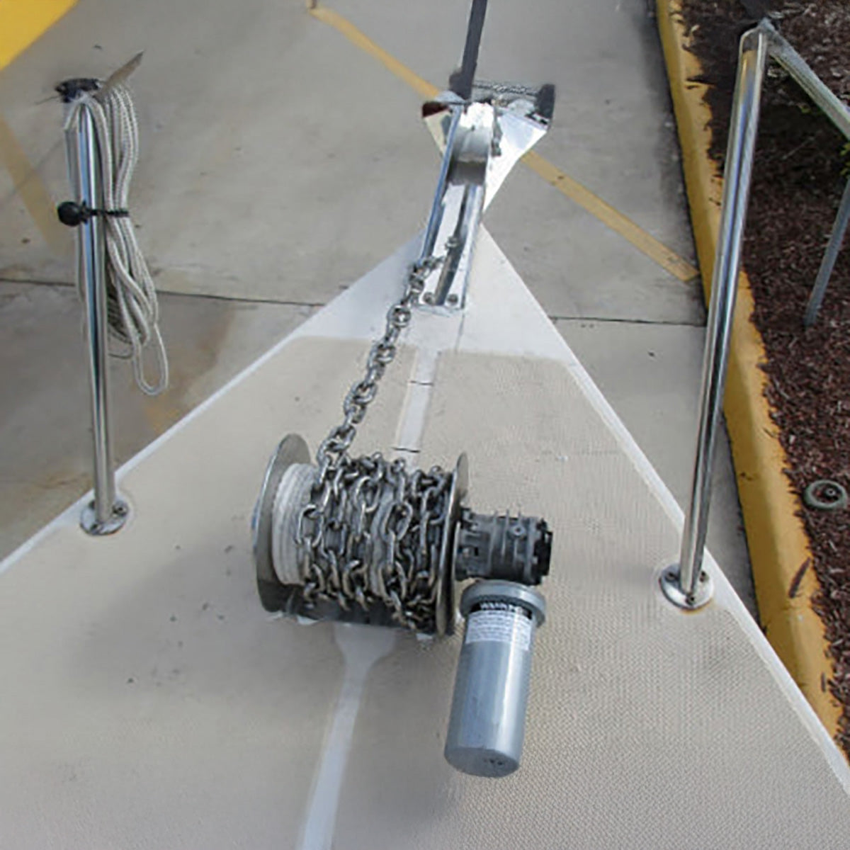 An anchor winch with a silver aluminum drum and a gray motor housing labeled 'SAILOR', featuring electrical wiring and a black handle.